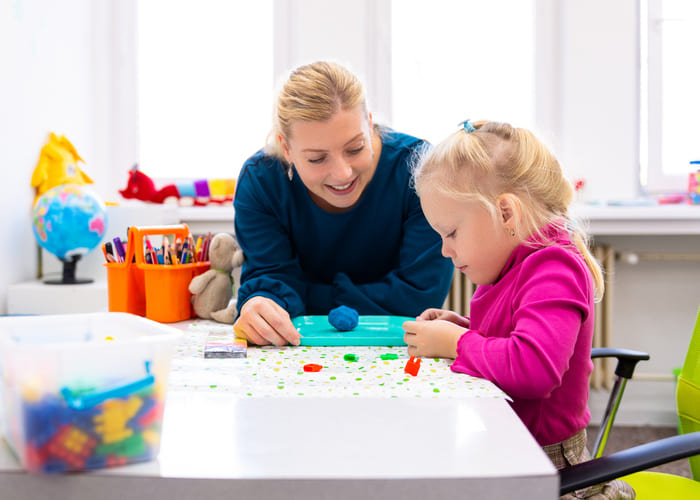 Toddler girl in child occupational therapy session doing sensory playful exercises with her therapist.