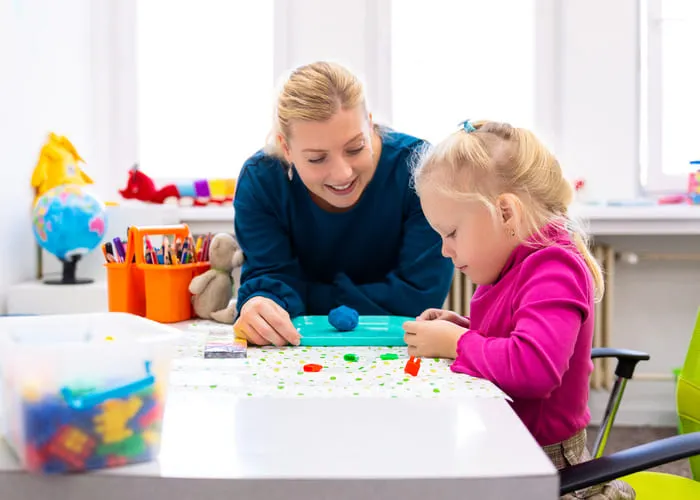 Toddler girl in child occupational therapy session doing sensory playful exercises with her therapist.