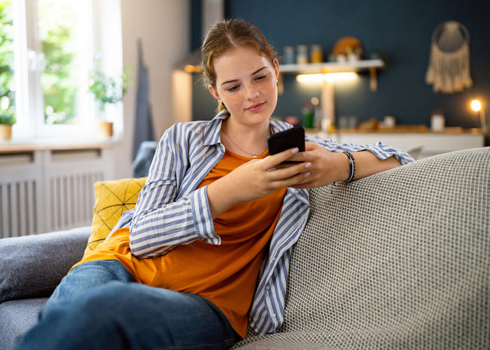 Redhead Caucasian teenage girl, using mobile phone, while sitting on the sofa in the living room