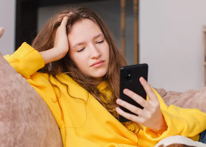 Upset young woman sit on couch at home hold smartphone receive unpleasant breakup text message, sad teen girl on sofa feel down read bad news on cellphone online, think of problem solution